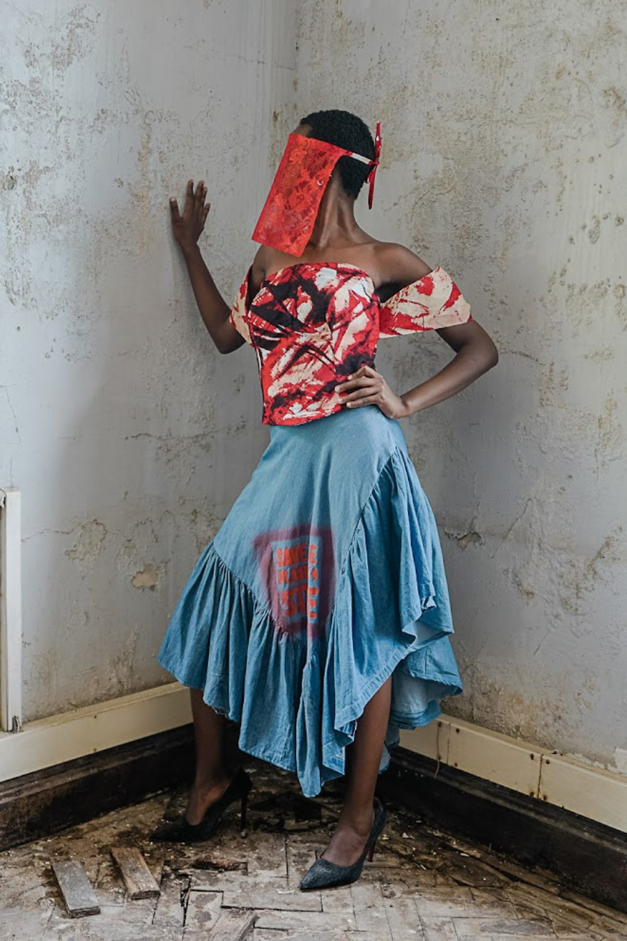 Woman in a colorful top and blue skirt standing in an abandoned room.