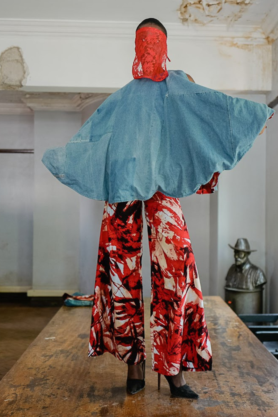 Person wearing a blue cape and red floral pants in an indoor setting