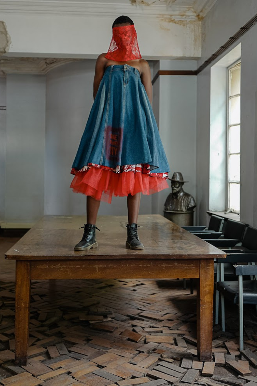 Person wearing a blue and red dress standing on a table in an abandoned room.