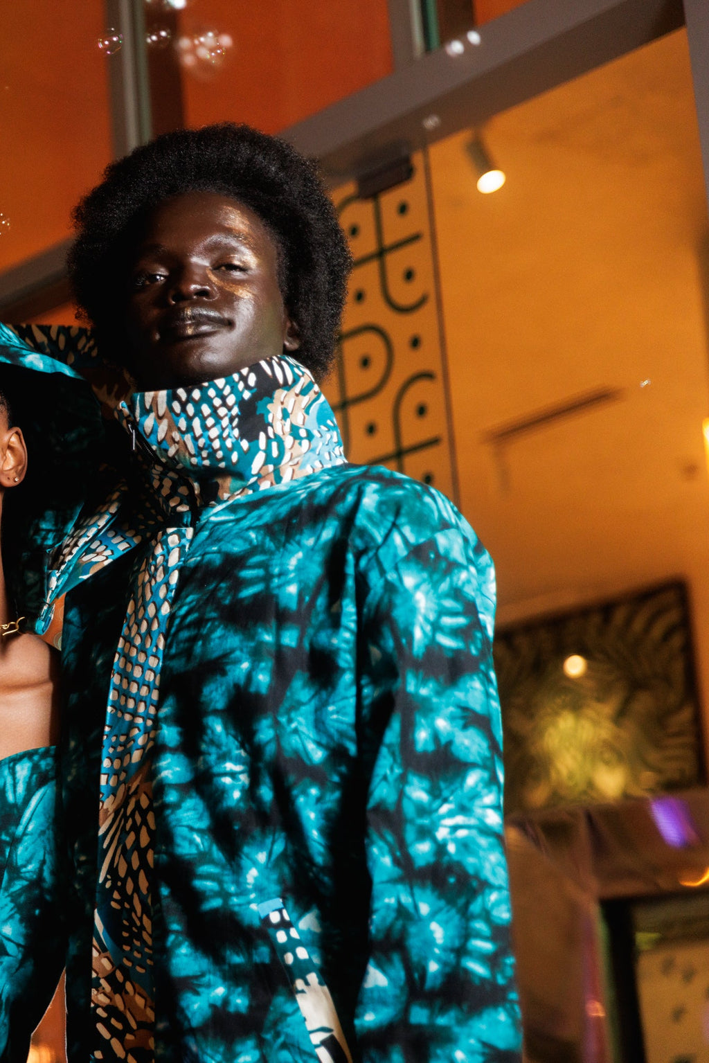 Two women in matching blue and black outfits with a decorative background