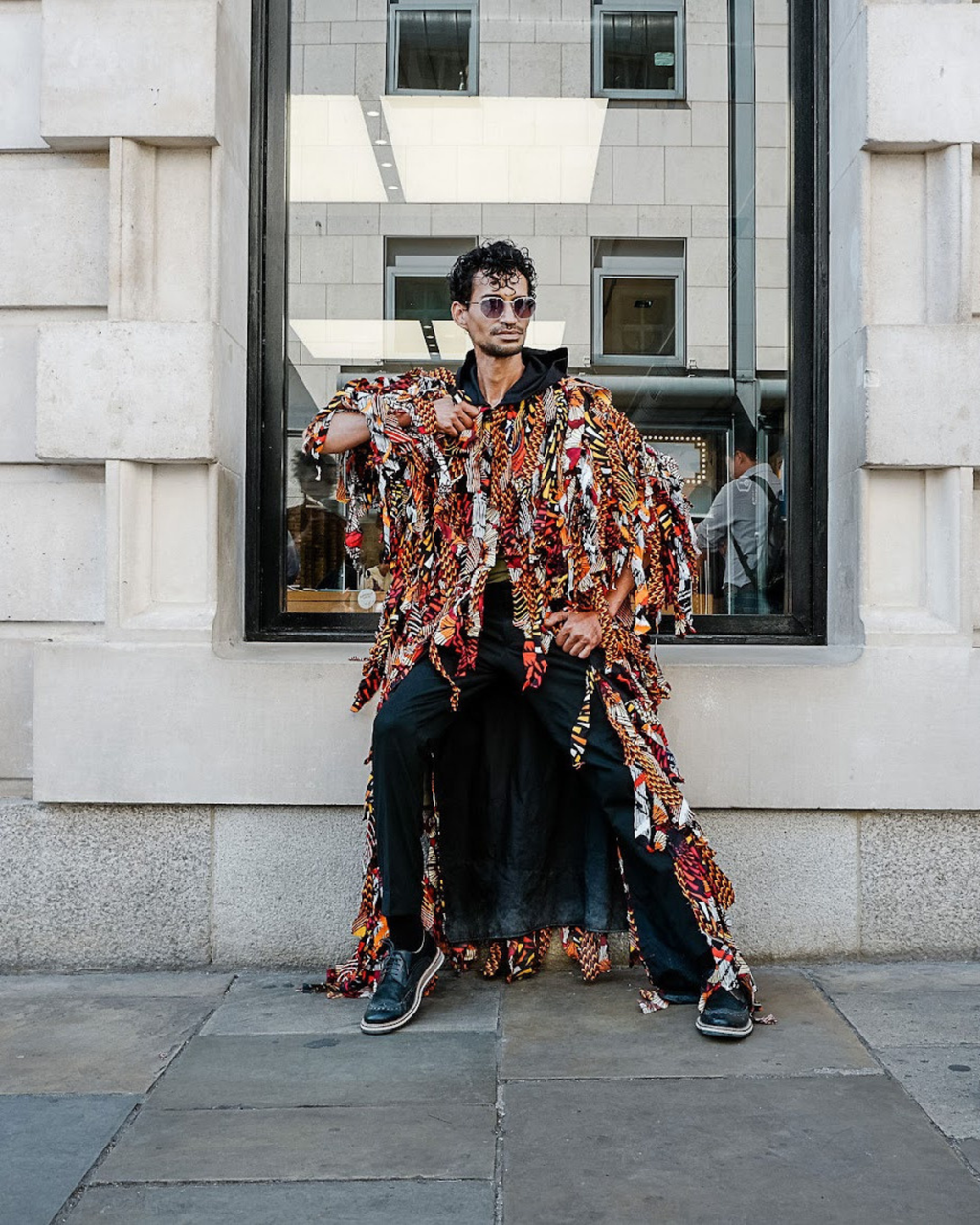 Person wearing a colorful patterned coat sitting on a wall with a building in the background
