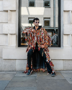 Person wearing a colorful patterned coat sitting on a wall with a building in the background