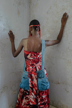 Person wearing a red and black patterned dress with blue denim accents against a plain wall.